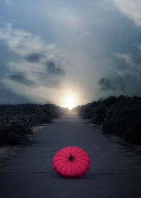 a red umbrella on a long rural road