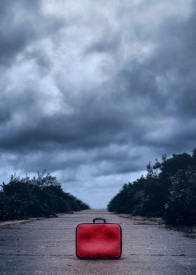 a red suitcase on a rural road