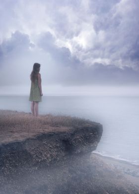 a girl standing on the edgle of a cliff over a foggy se ... 