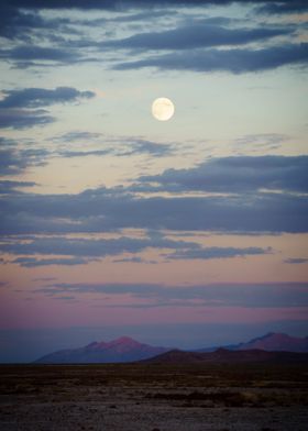 the moon rises over mountains in the desert.