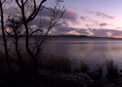 a low fog hangs above the loch as the sun slowly sets