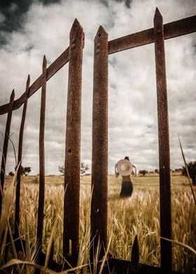 Rusty gate in a hay field with a woman wearing a big ha ... 