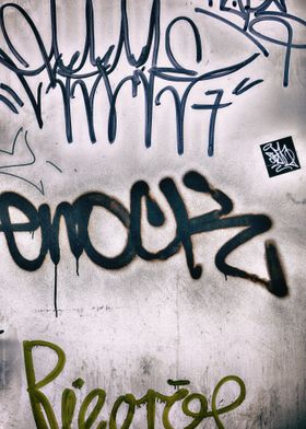 Closeup of graffiti tags on dirty white wall.