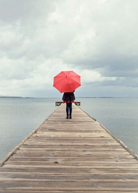 Girl standing n a pier with red umbrella.