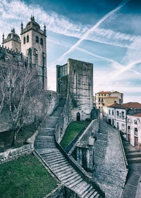 Porto, Portugal. Medieval Cathedral or Se Catedral do Porto, and tower that served as the old City-Hall - Antiga Casa da Camara. A photograph captures a winding stone staircase leading up to a grand cathedral made of weathered stone with tall towers.