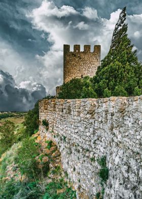 Medieval Castle of Sesimbra, Portugal, during a storm. The wall and watchtower with crenellations have as background the agricultural fields in the valley. Weathered stone wall with yellow moss and lichen, giving it a sense of age and history.