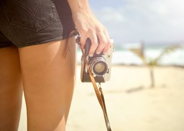 Woman holding a camera on the beach.